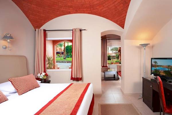 Innenansicht eines Zimmers im Jaz Makadi Oasis Resort & Club mit einem Bett, Fernseher, Schreibtisch und einem Ausblick auf den Garten.