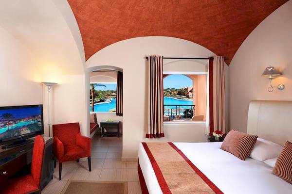 Hotelzimmer im Jaz Makadi Oasis Resort & Club mit Fernseher, roten Stühlen und Ausblick auf den Pool.