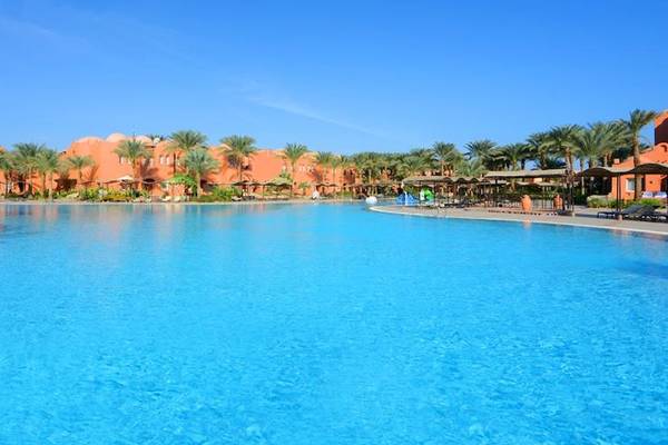 Außenpool im Jaz Makadi Oasis Resort & Club mit braunen Gebäuden und Palmen.