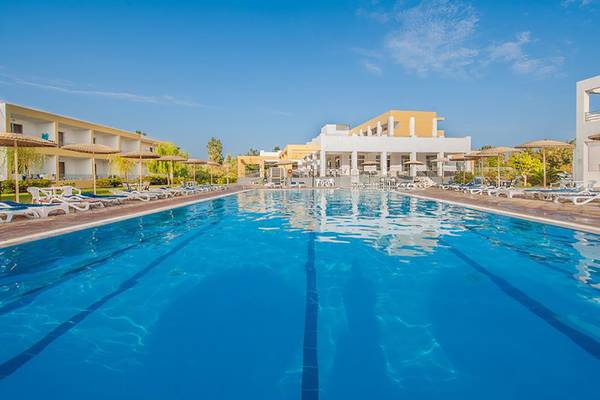Außenpool des Pyli Bay Hotels mit weißen Sonnenliegen und gelben Gebäuden im Hintergrund.