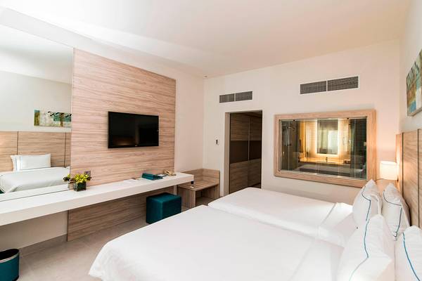 Innenansicht eines Doppelzimmers im Habtoor Grand Resort & Spa mit zwei Betten, Schreibtisch und Fernseher.