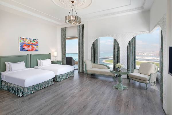 Innenansicht der Suite im Habtoor Grand Resort & Spa mit zwei Betten, Sofa und Blick auf das Meer.