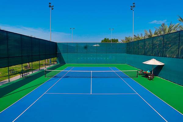 Tennisplatz im Habtoor Grand Resort & Spa mit blauer und grüner Begrenzung und einer Sonnenschirm.