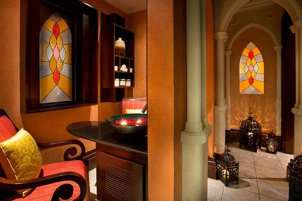 Innenansicht des Habtoor Grand Resort & Spa mit gemusterten Fenstern, einem Tisch mit Rosenblättern und illuminierten Laternen.
