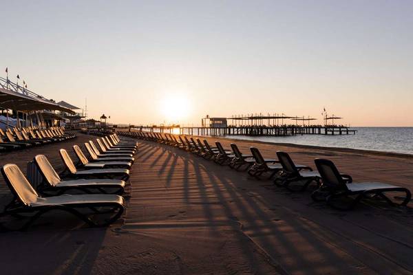 Strand des Susesi Luxury Resort bei Sonnenuntergang mit vielen Liegen in einer Reihe.
