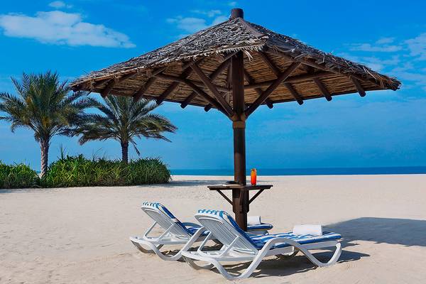 Sonnenliegen unter einem Sonnenschirm auf dem weißen Sandstrand des Habtoor Grand Resort & Spa.