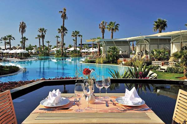 Außentisch am Susesi Luxury Resort Pool mit Blick auf Palmen und Gebäude.