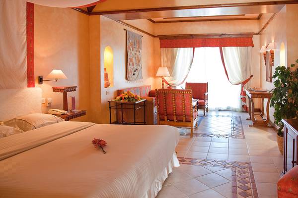 Schlafzimmer im Grand Resort Hurghada mit Bett, Nachttischen, Lampen und Wohnzimmerbereich.