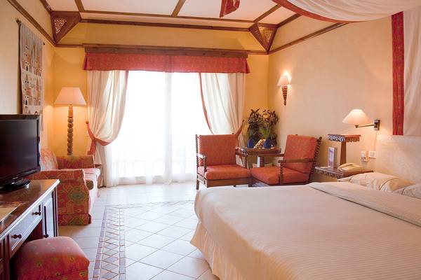 Hotelzimmer im Grand Resort Hurghada mit Bett, Sesseln, Fernseher und Tischlampe.
