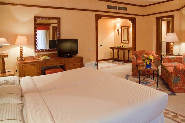 Doppelzimmer im Grand Resort Hurghada mit zwei Betten, Fernseher, Tisch mit Lampe, und Sessel.
