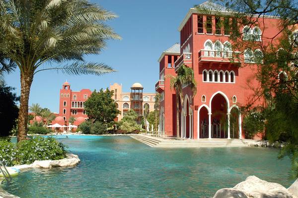Außenansicht des Grand Resort Hurghada mit rotem Gebäude, Palmen und Swimmingpool