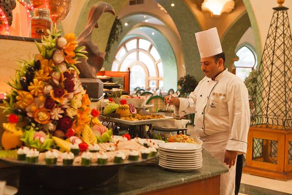 Ein Koch steht bei einem großen Speisenbuffet im Grand Resort Hurghada und serviert verschiedene Gerichte.