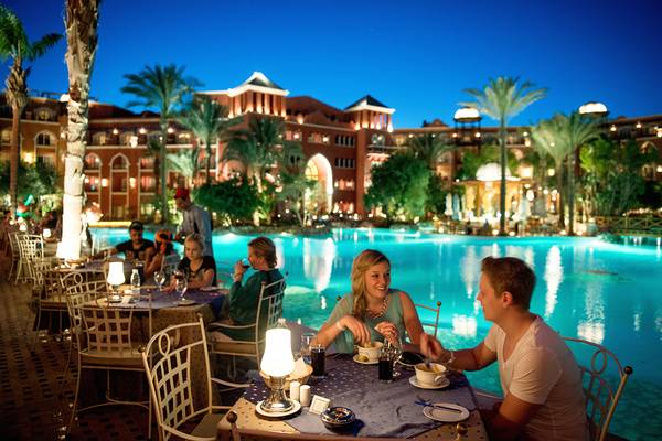 Hotelgäste essen am Pool im Freien, während sie das Hotelgebäude im Hintergrund betrachten.
