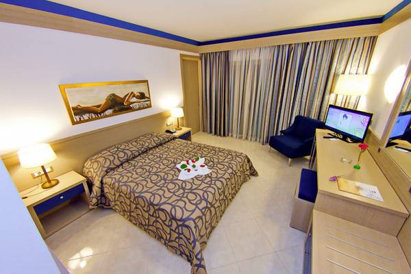 Ein Zimmer im Nana Golden Beach Hotel mit einem Doppelbett, Nachttischen, Fernseher und einem Gemälde an der Wand.