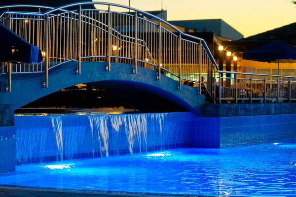 Ein blau beleuchteter Pool mit einer Brücke und Wasserfällen bei Nacht im Nana Golden Beach Hotel.