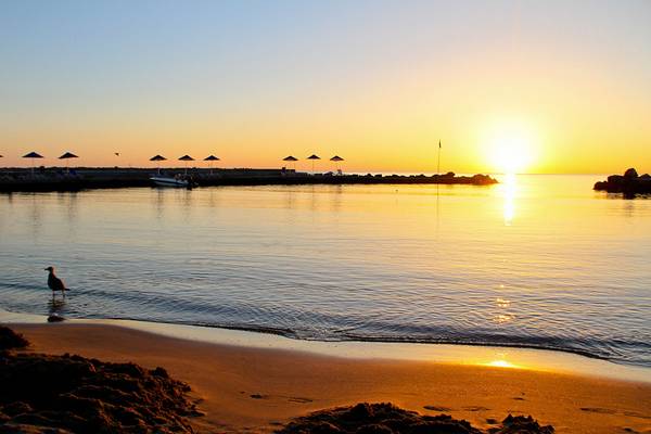 Sonnenuntergang am Nana Golden Beach mit einem Vogel im Wasser und einem Boot im Hintergrund.