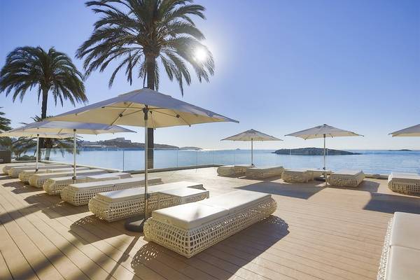 Terrasse mit Sonnenliegen und Sonnenschirmen am Strand mit Blick auf das Meer und Palmen