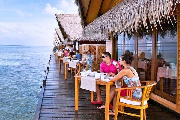 Meerblick-Restaurant im Hotel Adaaran Select Hudhuran Fushi mit Gästen, die am Tisch sitzen.