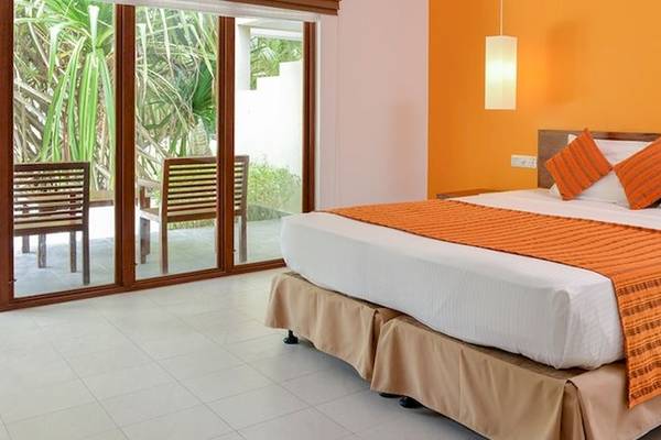 Hotelzimmer im Adaaran Select Hudhuran Fushi mit weißem Bett, orangen Kissen und Tisch neben dem Bett.
