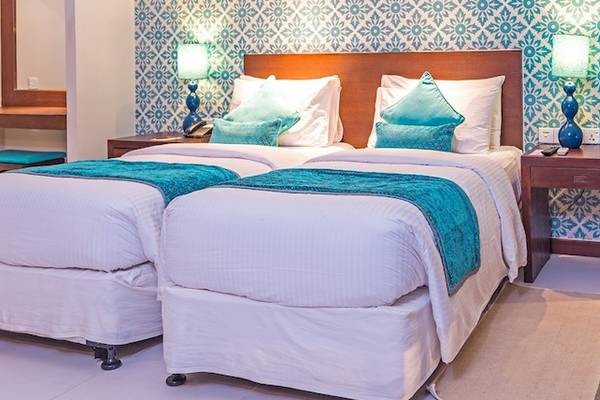 Doppelbettzimmer im Adaaran Select Hudhuran Fushi mit blauen und weißen Musterwänden, zwei Betten, Tischlampen und Obstteller.