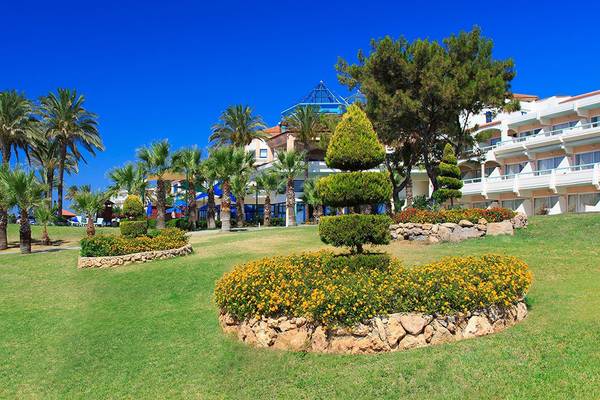 Grüne Rasenfläche vor dem Rodos Princess Beach Hotel, gesäumt von Palmen und Blumenbeeten.