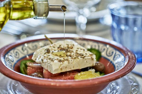 Olivenöl wird auf einen griechischen Salat in einer Schüssel gegossen.
