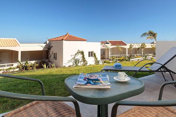 Außenbereich des Rodos Princess Beach Hotels mit Garten, Liegestühlen und Gebäuden im Hintergrund.