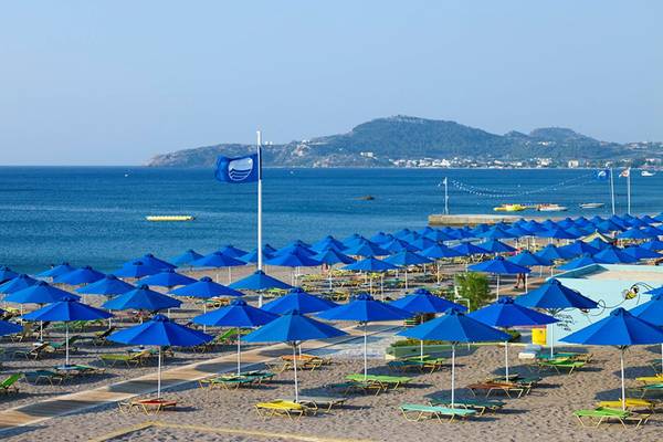 Strand mit vielen blauen Sonnenschirmen und Liegen vor einem ruhigen Meer