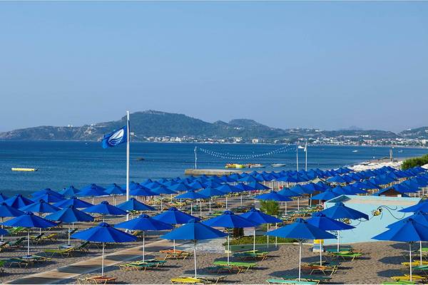 Strand mit blauen Sonnenhüten und Blick auf das Meer und Berge im Hintergrund.