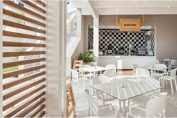 Innenansicht des Junior Bars im Esperides Beach Resort mit weißen Tischen und Stühlen.