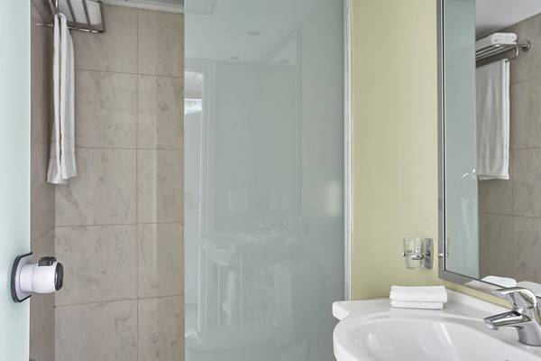 Badezimmer im Esperides Beach Resort mit Glasdusche, Waschbecken und Spiegel.