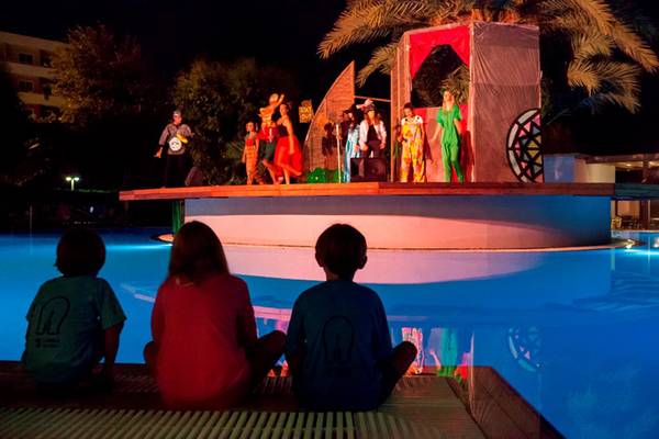 Kinder beobachten eine Theateraufführung am Pool des Esperides Beach Resorts bei Nacht.
