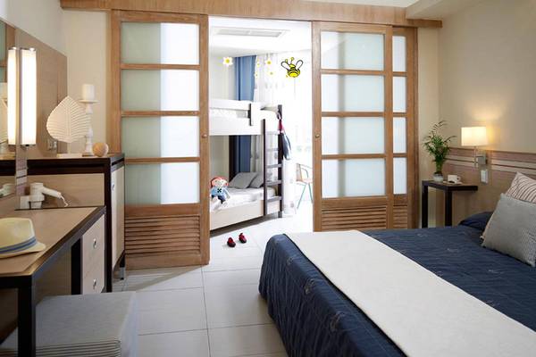 Doppelzimmer im Esperides Beach Resort mit Doppelbett, Nachttisch, Schreibtisch, Spiegel, Lampe und offenen Schiebetüren zu einem Schlafbereich mit Etagenbett.