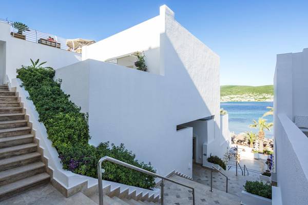 Außenansicht des weißen Privé Hotel Bodrum mit Treppen, Pflanzen und Meer im Hintergrund