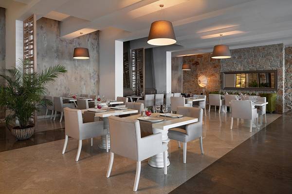 Innenbereich des Restaurants im Prive Hotel Bodrum mit weißen Tischen und Stühlen, Steinwänden und Hängelampen.