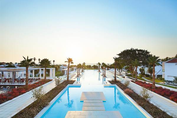 Gesamtansicht des Poolbereichs des Grecotel Lux Me Dama Dama Hotels mit blauem Wasser und weißen Gebäuden.