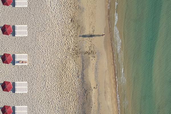 Luftaufnahme eines Luxushotels am Strand mit roten Sonnenschirmen und einer Person, die ins Wasser geht.