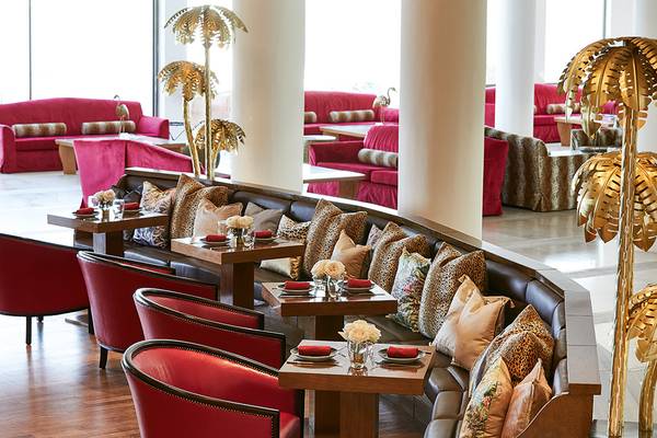 Innenbereich des Grecotel Lux Me Dama Dama Hotels mit roten Möbeln und goldenen Palmen.