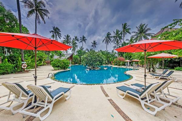 Außenpoolbereich des Duangjitt Resort & Spa mit roten Sonnenschirmen und weißen Liegestühlen.