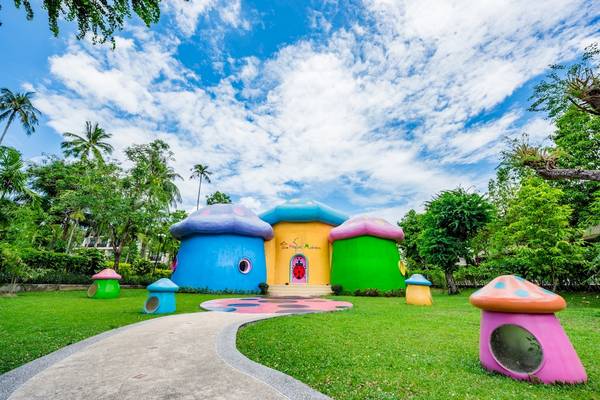 Außenansicht des Duangjitt Resort & Spa mit farbenfrohen Pilzhäusern und bunten Pilzskulpturen auf dem Rasen.
