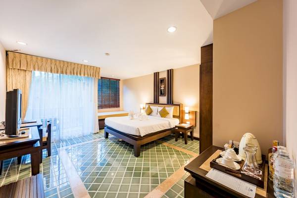 Hotelzimmer im Duangjitt Resort & Spa mit grünen Fliesen, einem Bett, Fernseher und Schreibtisch.