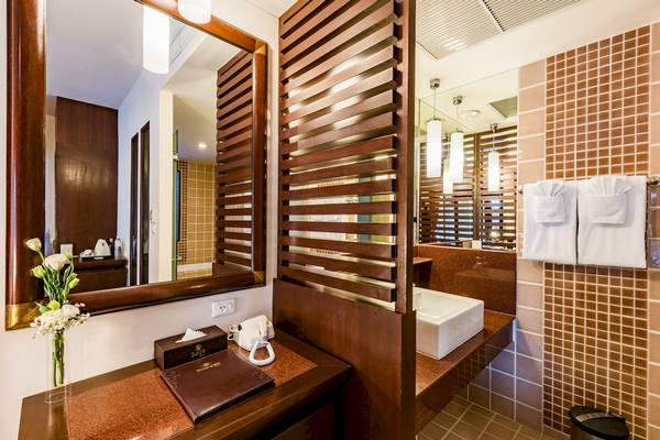 Badezimmer im Duangjitt Resort & Spa Hotel mit Spiegel, Blumenvase, Telefon und Waschbecken.