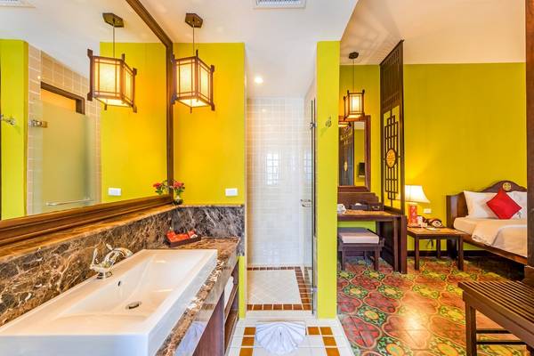 Innenansicht des Badezimmers im Duangjitt Resort & Spa mit gelben Wänden, einer Badewanne und einem Waschbecken.