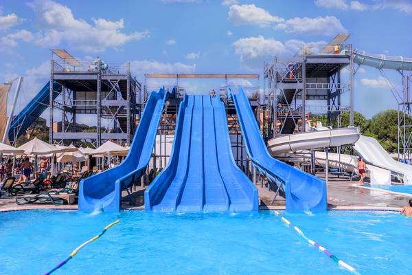 Mehrere blaue Wasserrutschen im Atrium Family Resort Belek mit mehreren Personen, die darauf warten, herunterzurutschen.