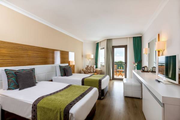 Zwei Betten im Hotelzimmer des Asteria Family Resort Belek mit Balkon und Blick auf den Garten.