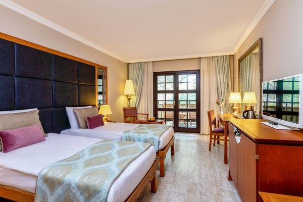 Zwei Betten in einem Hotelzimmer im Asteria Family Resort Belek, mit einem Fernseher und einem Schreibtisch.