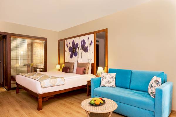 Innenansicht eines Hotelzimmers im Asteria Family Resort Belek mit einem Bett, Sofa und Tisch mit Früchten.