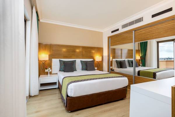 Innenansicht eines Schlafzimmers im Asteria Family Resort Belek mit einem Doppelbett, Nachttischen und einem Spiegel.