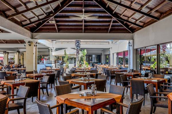 Innenbereich des Asteria Family Resort Belek mit vielen Tischen und Stühlen, Deckenventilator und Palmen.