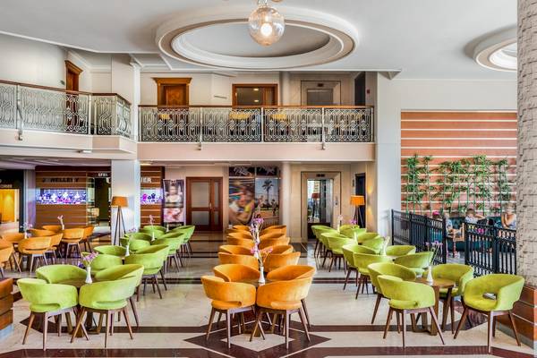 Lobby des Asteria Family Resort Belek mit grünen und orangen Stühlen und Tischen.